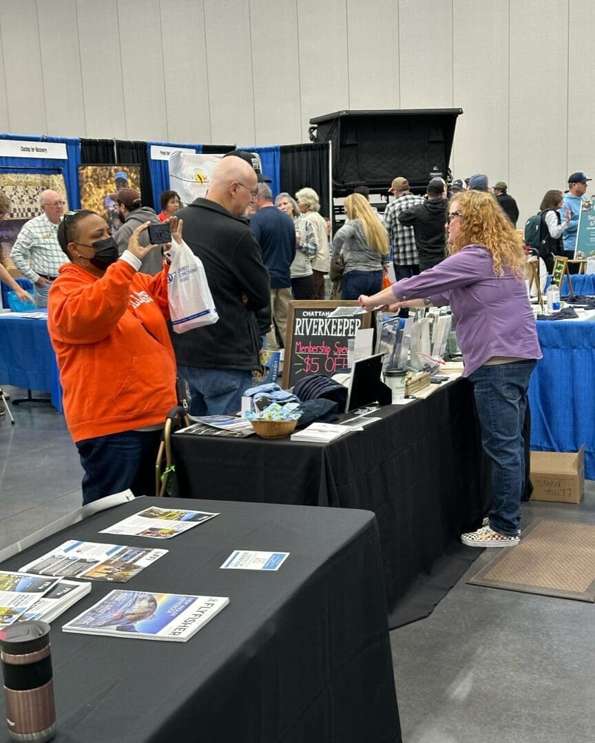 A woman in a purple shirt talks to a man at an exhibition booth labeled 