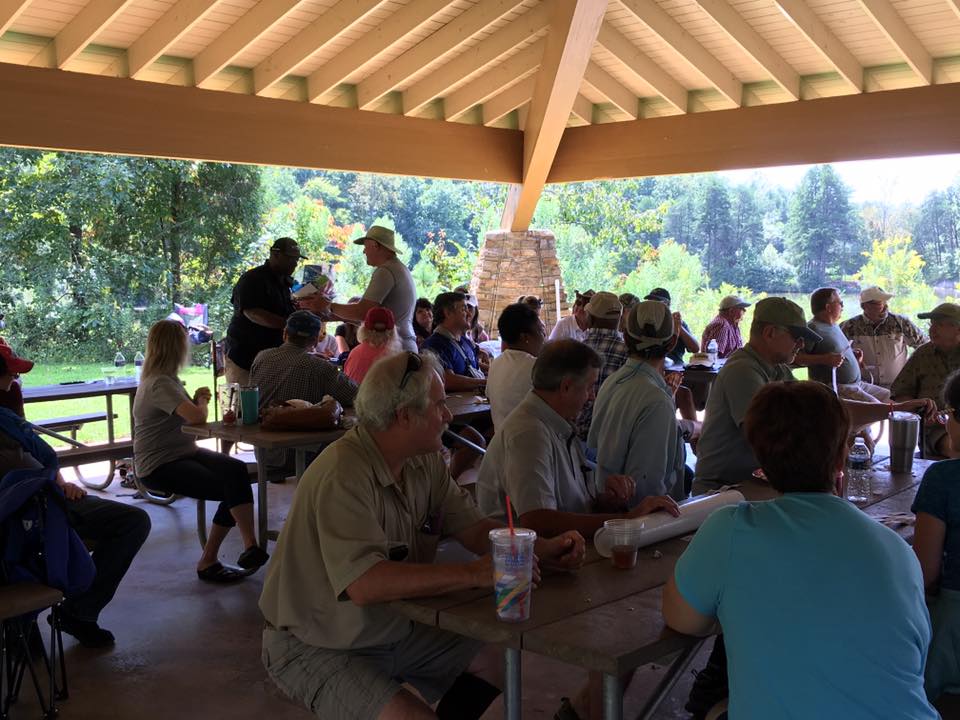 A group of people sitting at picnic tables under a pavilion in a park, engaging in conversation and activities.